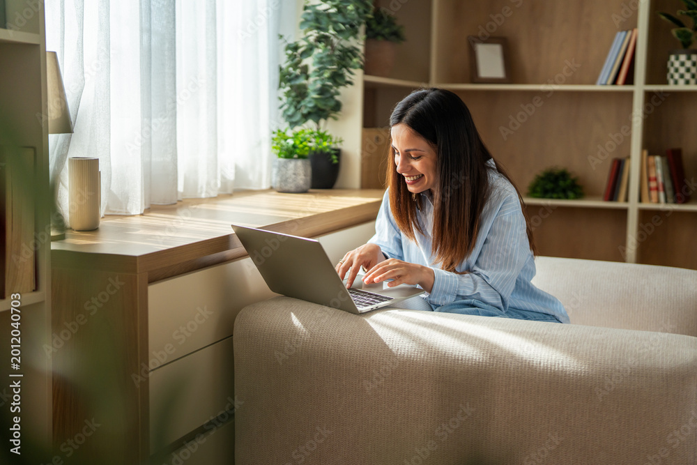 Obraz premium Smiling woman using laptop for remote work at home