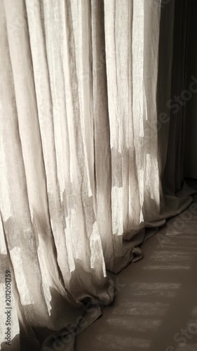 Cinematic shot of floor-to-ceiling beige linen curtains swaying gently in a modern interior. Warm morning sunlight filters through the semi-sheer fabric, casting soft shadows