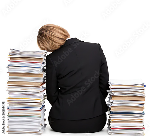 middle aged female employee in formal suit sleeping while seated back view surrounded by stacked paperwork isolated on white background