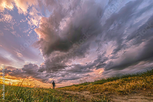 Quadro em tela Lone person standing under dramatic storm clouds in natural landscape at sunset