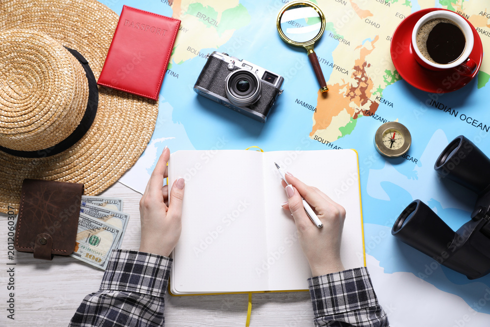Fototapeta premium Woman with notebook and world map planning trip at wooden table, top view