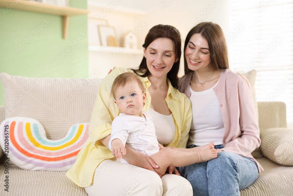 Fototapeta premium LGBT parents. Happy lesbian couple with their cute baby on sofa at home