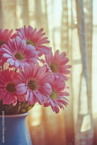 A blue vase filled with pink flowers sits next to a window, ideal for decorating your home or office vertical frame