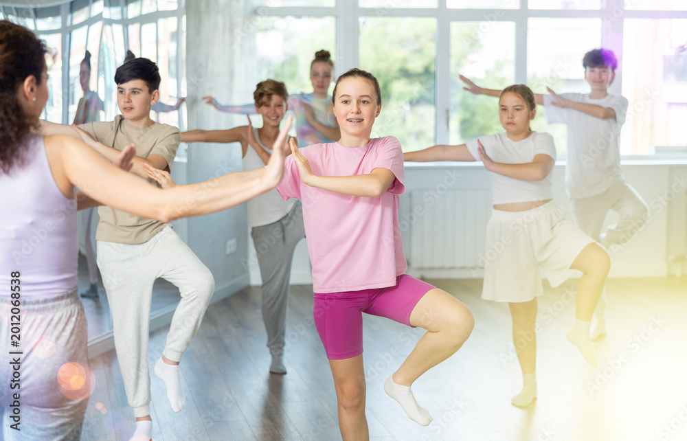 Fototapeta premium Girl teen performs modern dances repeats movements of unrecognizable teacher together with friends during lesson at choreographic school. Hobbies, active pastime