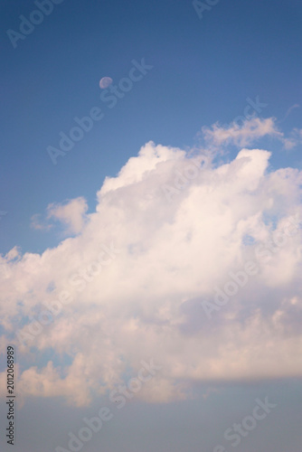 Fotografija Pale moon visible in a daytime blue sky with fluffy white clouds