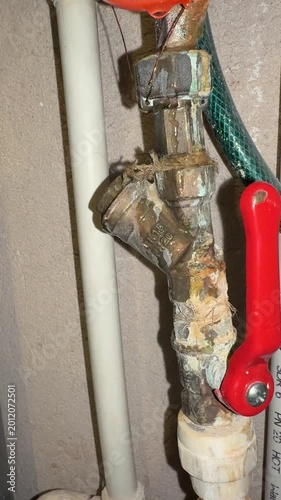 Corroded hot water meter connection leaking near red valve handle plumber inspecting closeup of calcified pipe joint with rust