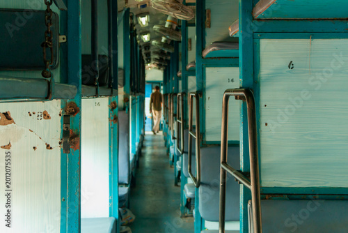 Perspective view inside an Indian sleeper class train featuring blue benches and ceiling fans