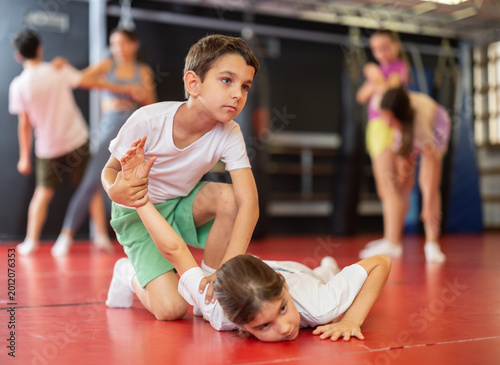 Teenage girl learns a hand grip in sparring with a boy during a workout. Children practice self-defense techniques in the gym