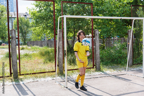 Photography Teen boy in yellow uniform balancing soccer ball on hand near outdoor goalpost
