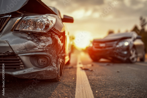 Two damaged vehicles after a road collision on an asphalt highway during sunset with visible dents and debris scattered on the ground between them