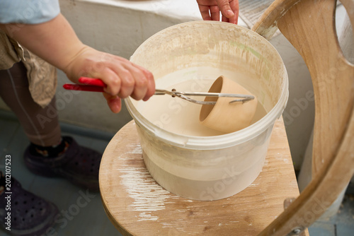 Close up view of a clay bowl being lowered into a container of liquid ceramic glaze.