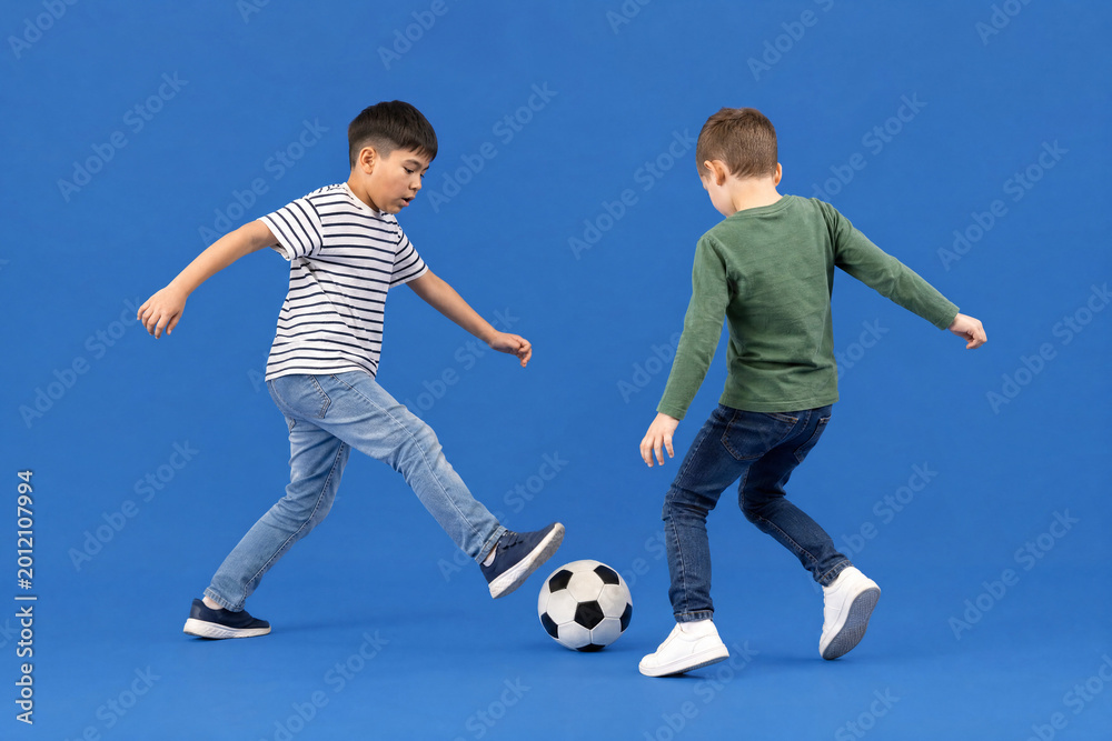 Obraz premium Two young boys playing soccer together in a studio with a blue background, childhood fun and physical activity for sports education and youth competition