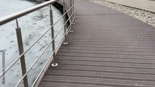 Icy reservoir jetty with steel railings, textured boardwalk and thin shore ice, overcast sky and muted tones, industrial detail