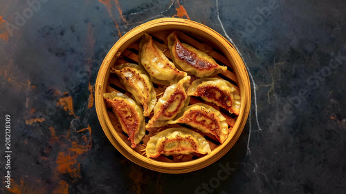 Quadro su tela Golden pan-fried Gyoza in a bamboo steamer on a dark marble surface