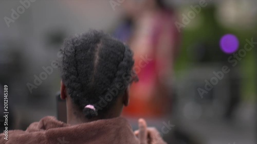 Woman dances in time to music cell phone video rear view hair braids