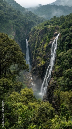 Majestic twin waterfalls cascading down lush green cliffs surrounded by dense tropical rainforest under misty overcast skies in a serene natural landscape