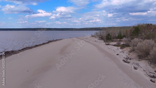 Photos A wide strip of sandy beach on the shore of a large lake and bare forest on a cloudy day in early spring, photographed from above