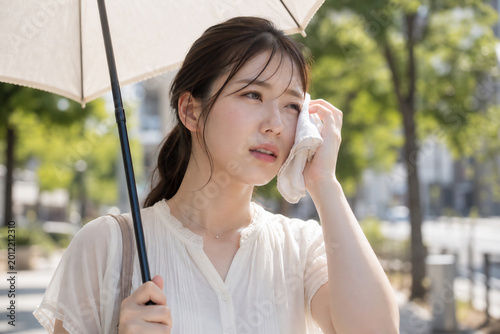 夏の猛暑に日傘を差し汗を拭く若い日本人女性、熱中症対策、酷暑、紫外線、ライフスタイル、Generative AI