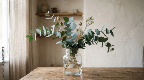 A vase with eucalyptus branches on a wooden table in a cozy, minimalist kitchen setting.