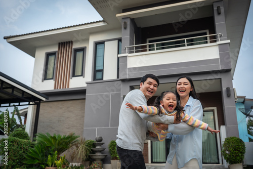 happy family, cheerful father and mother playing airplane with child girl while standing in front of their house