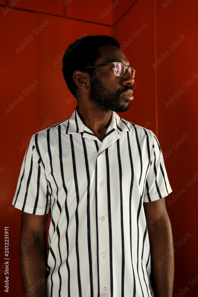 Fototapeta premium Black man standing against red wall contemplating