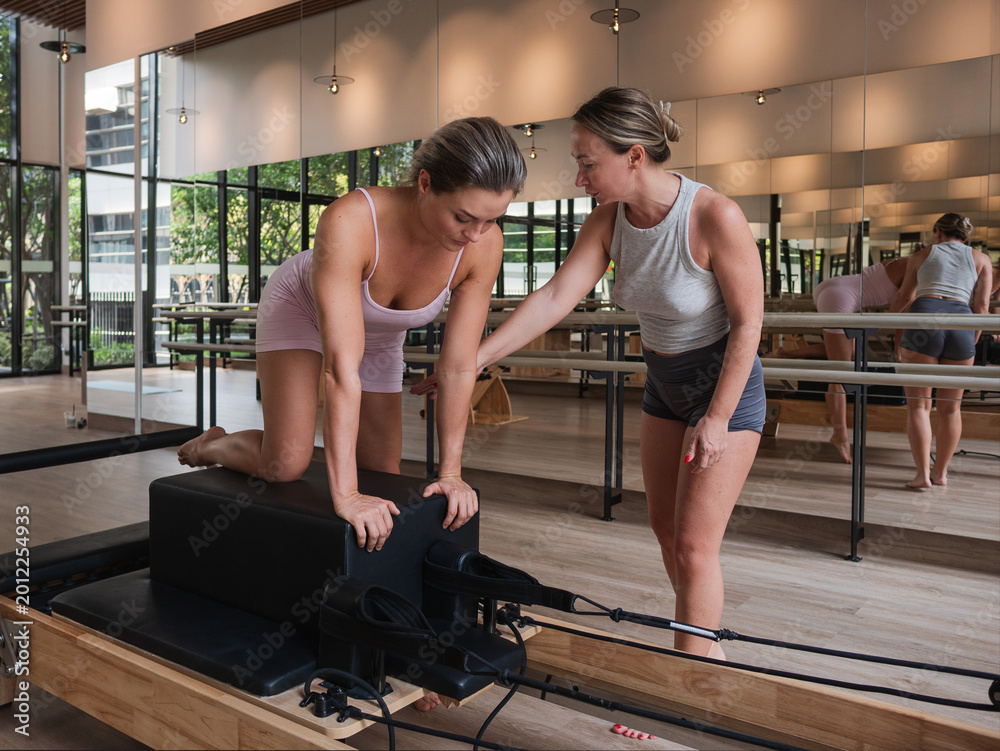 Fototapeta premium Pilates instructor assisting woman on reformer machine in modern fitness studio,