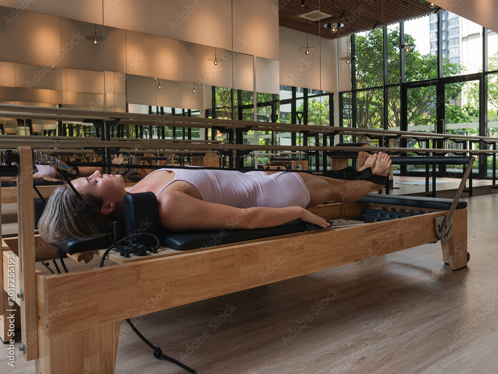 Fototapeta premium Woman performing leg press and core stability exercises on Pilates reformer machine in modern fitness studio