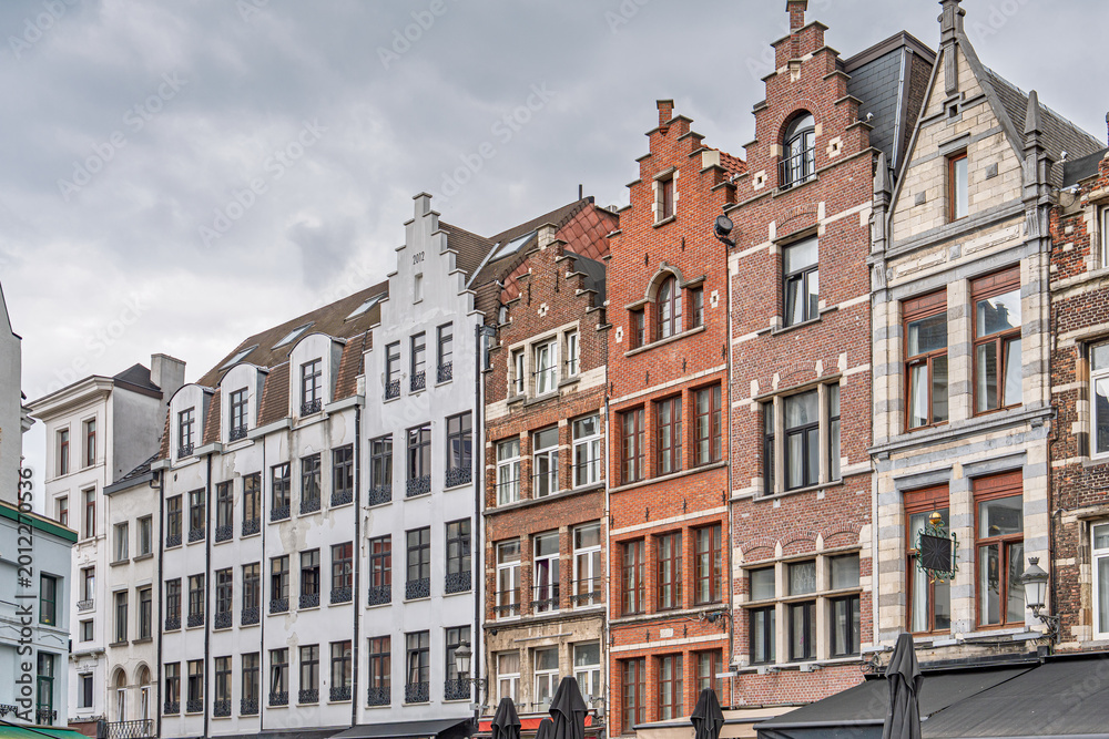 Obraz premium A row of traditional buildings in Antwerp displays the citys rich architectural heritage, with historic facades aligned along a charming street beneath a cloudy sky.