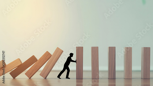 A silhouette of a man pushing a domino to stop a falling sequence of wooden blocks on a shiny floor with a gradient background