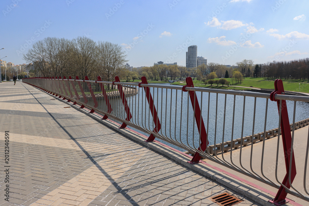 Obraz premium Red railings line a paved walkway beside a calm river