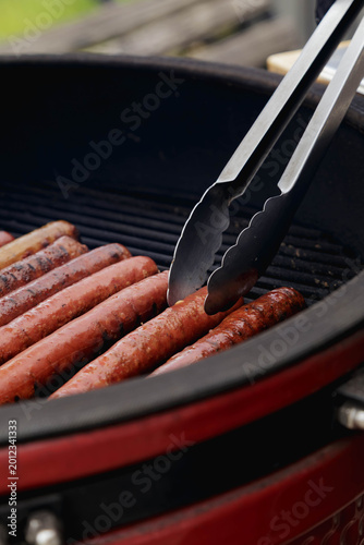 Close-up of sausages being grilled with tongs on a round BBQ