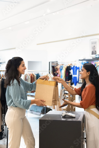 Obraz na płótnie Cheerful shop assistant hands over two eco-friendly paper bags with recent purchases to delighted female customer