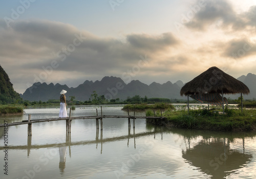 Female traveler walking on a small bamboo bridge over a pond in the karst landscape of Phong Nha National Park area, Vietnam.
