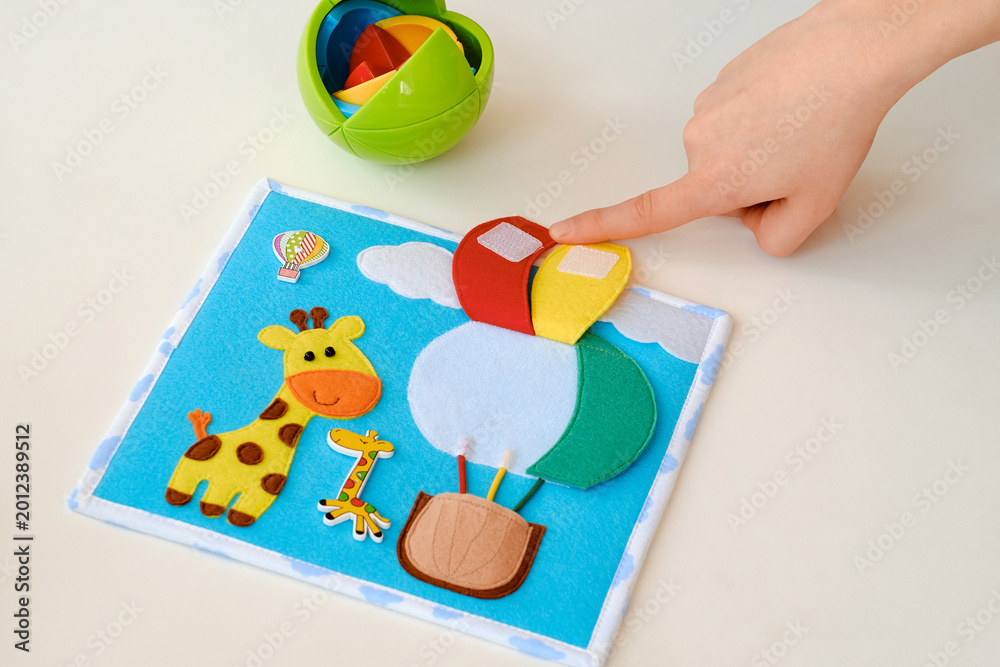 Obraz premium Child playing with colorful felt activity board featuring giraffe and hot air balloon, fine motor skills educational toy on white background