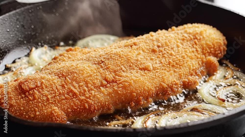 Crispy Breaded Fish Fillet Sizzling in a Hot Skillet with Onions.