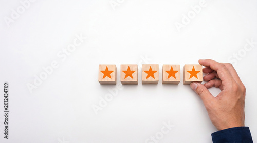 Five-Star Customer Delight: An individual's hand delicately places wooden blocks adorned with star icons, symbolizing a perfect customer satisfaction score.