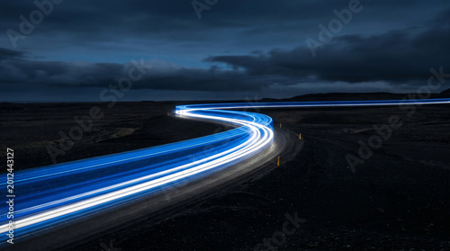 Blue light trails on a winding road at dusk under a cloudy sky