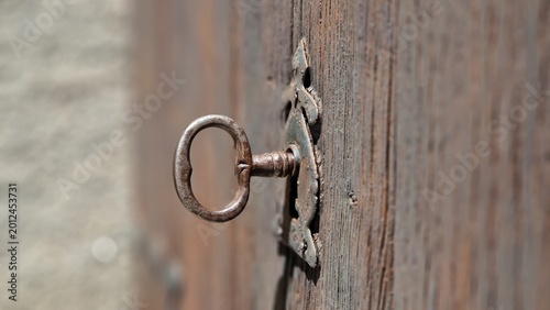 Old rusty key inserted into vintage keyhole on weathered wooden door