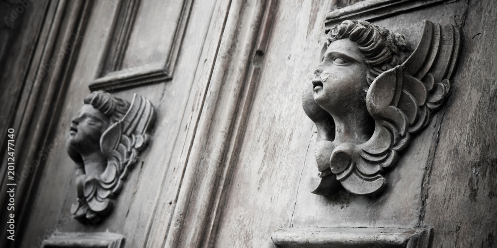 Fototapeta premium Sculpture of an old wooden angel against a wooden door of a church - more than 100 years old
