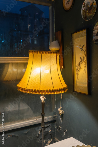 Vintage floor lamp with yellow fringed lampshade in a dark interior. Solitary warm light of a classic lamp as a metaphor for hope and domestic sanctuary.