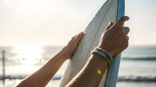 Surfer holding a surfboard on the beach at sunset