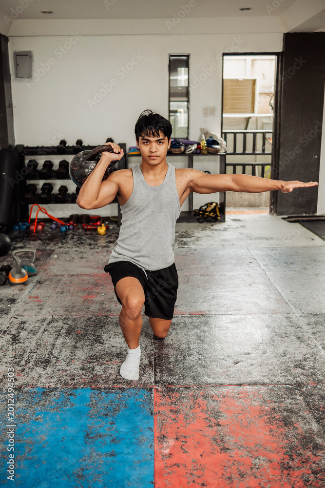 Fototapeta premium Young man performs a half kneeling kettlebell stability exercise to improve shoulder strength, balance, coordination and core control in gym