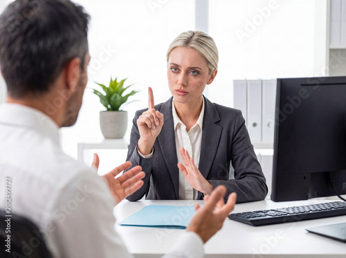 Tableau sur toile Serious blonde businesswoman sternly warns male colleague, gesturing with finger to emphasize a point
