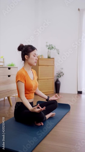 young Asian women meditation yoga lotus pose mindfulness breathing exercise wellness practice relax peaceful morning routine home living room wooden floor mat
