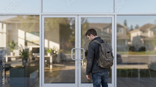 first home buyer loan stress concept. Young man with backpack standing in front of glass doors of a modern building