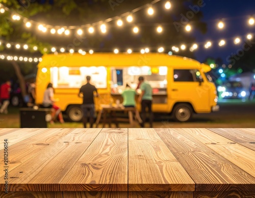 A wooden table foregrounds a food truck at night
