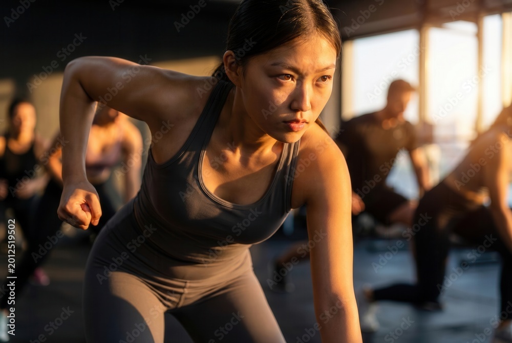 Fototapeta premium Woman focusing on her fitness goals while performing an active exercise in a gym with others