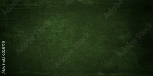 An aged and empty green chalkboard with a rough grunge texture provides a dark vintage surface for a blank backdrop or wallpaper pattern