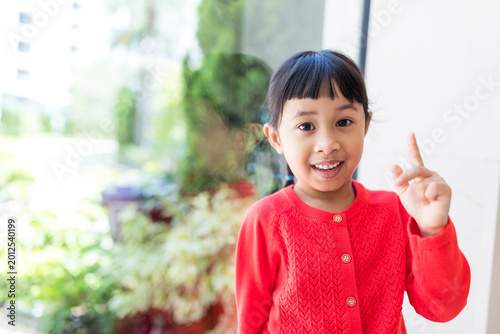 Asian little girl smiling with her index finger pointing up