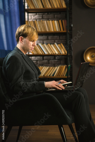 Focused Young Businessman in Suit Working on Laptop in Home Office Library with Bookshelves